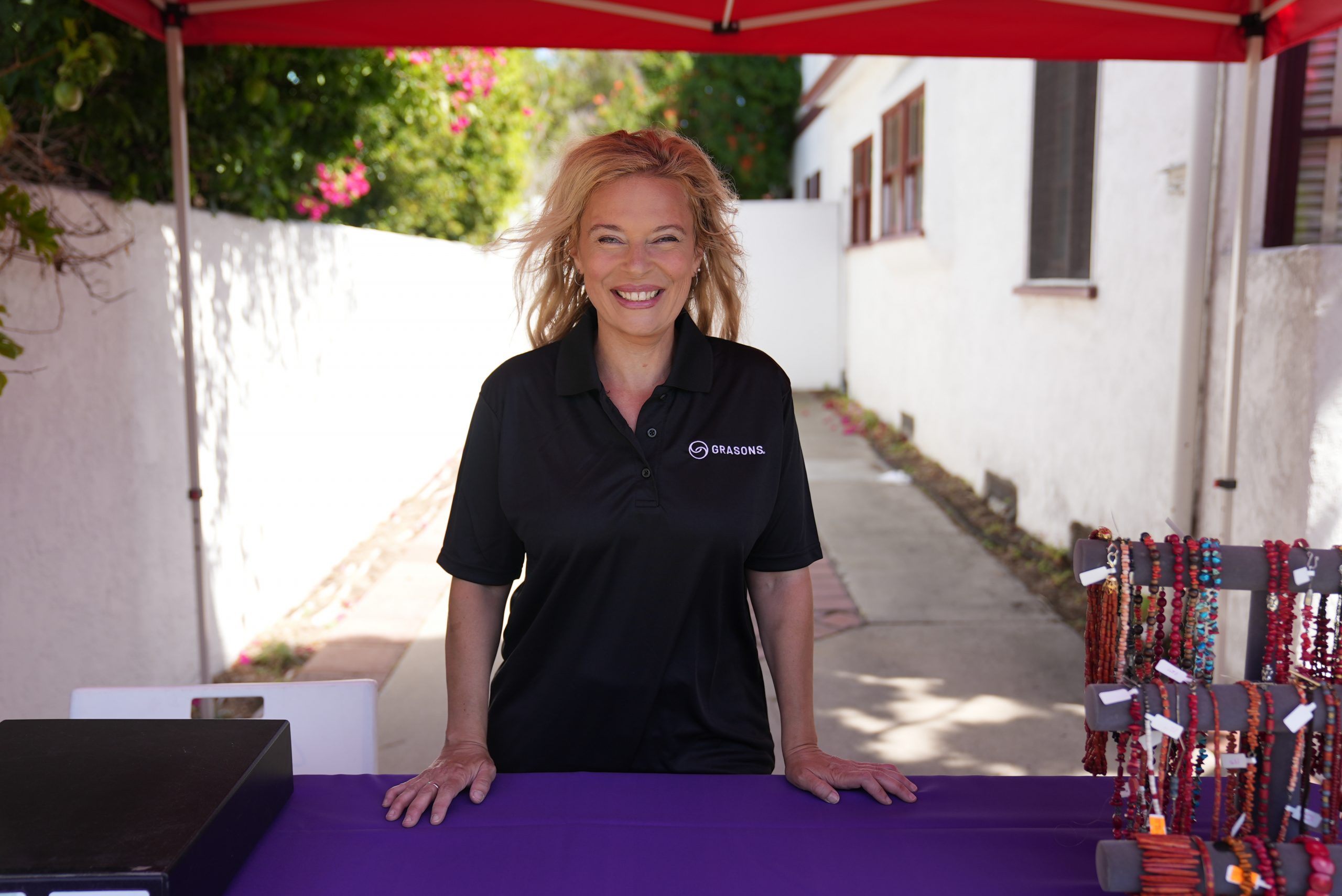 A female Grasons employee smiles behind an outdoor booth for selling jewelry.