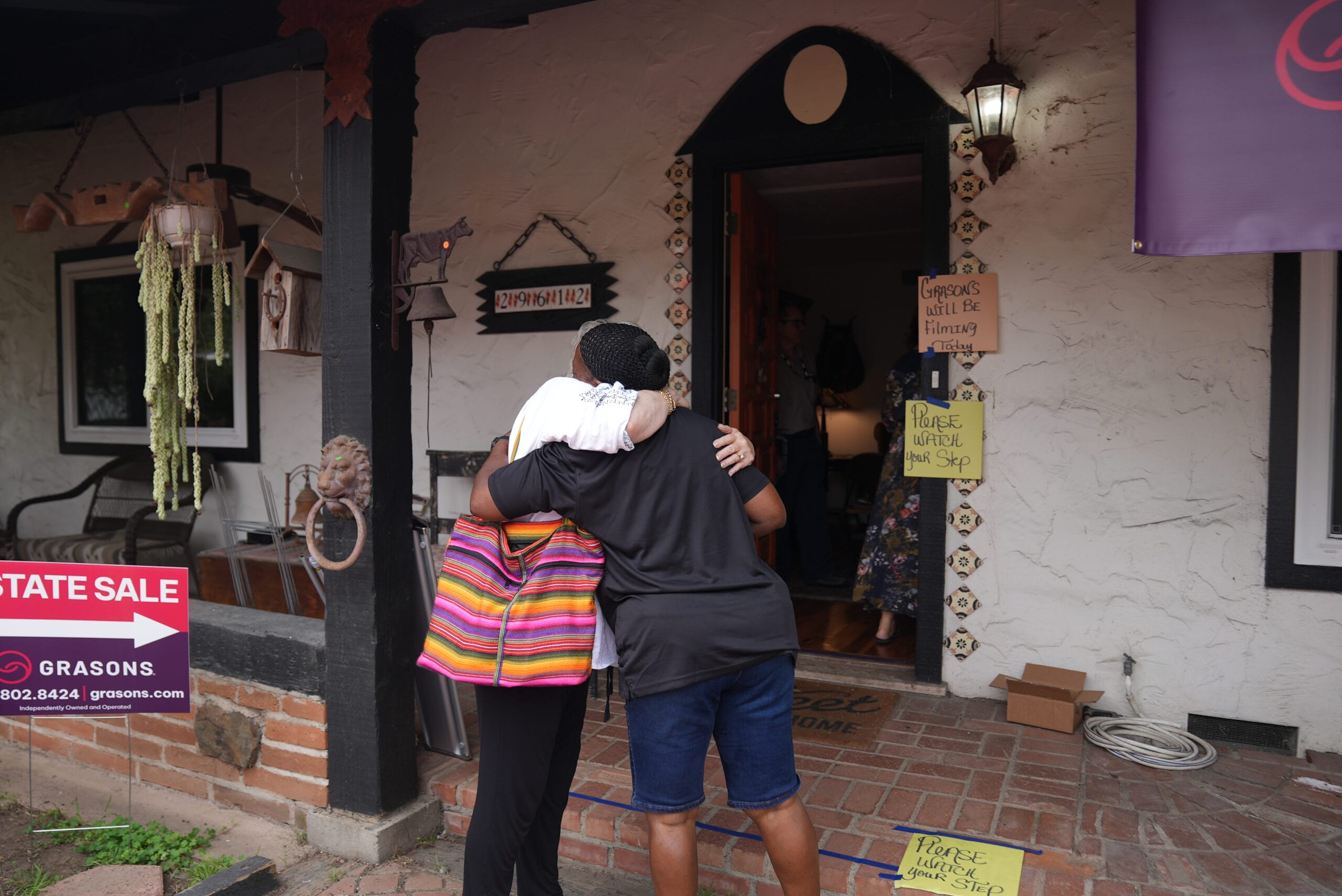 Two people hug in front of a home hosting an estate sale